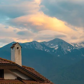 Clouds in the rays of the setting sun against the background of the tiled roof Stock Photos