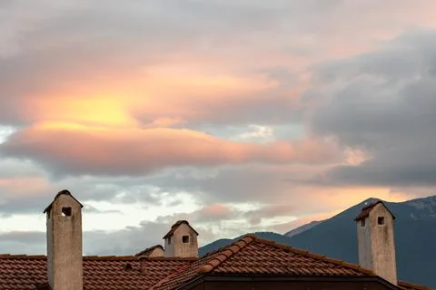 Clouds in the rays of the setting sun against the background of the tiled roof Stock Photos