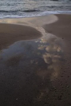 Clouds reflect in a shallow pool on the shore beside the sea Stock Photos