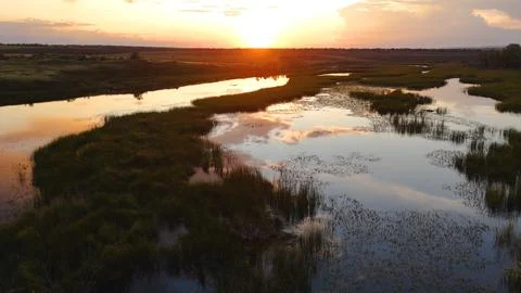 Clouds reflected in a reed-covered lake at a bright orange sunset Stock Photos