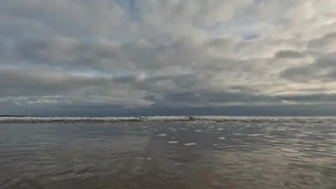 Clouds reflected in shallow water flowing over a flat sandy beach Stock Footage 303251949