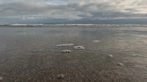 Clouds reflected in shallow water flowing over a flat sandy beach Stock Footage 303251950