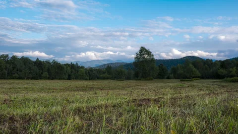 Clouds Roll Over Mountains with Field in Foreground Timelapse Stock Footage 250133272