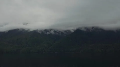 Clouds rolling over forested mountains above a dark channel Alaska Stock-Footage 347824052