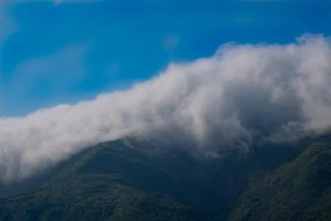Clouds rolling over green mountain slopes with blue sky Stock Photos