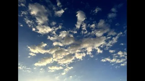 Clouds scatter across deep blue sky, soft white formations float gently Stock Photos