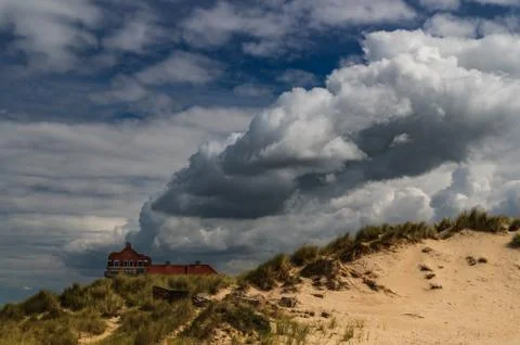 Clouds seem to come out of a building by dunes. Stock Photos