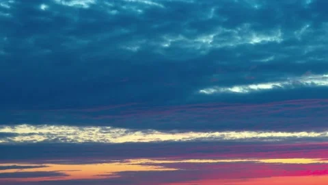 Clouds slowly float across the sky at sunset, illuminated by the rays of the set Stock Footage 220622289
