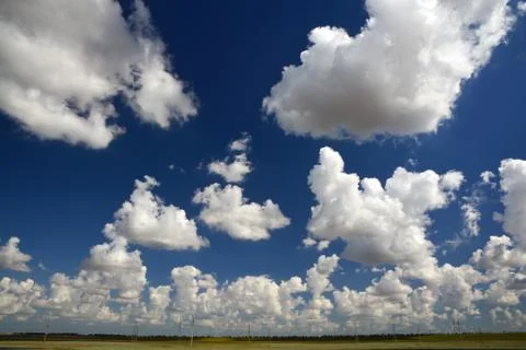 Clouds on a sunny day at blue sky. Landscape with electric poles in autumn field Stock Photos