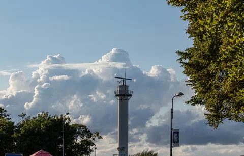 Clouds surround a tall tower on a clear day in an open area with trees Stock Photos