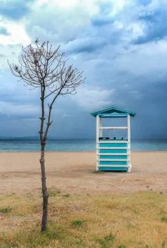 Cloudscape over the sea. Rescue tower and tree on the empty beach. Stock Photos