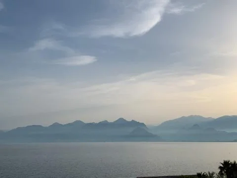 Cloudy blue sky over Mediterranean sea with mountains silhouettes. Stock Photos
