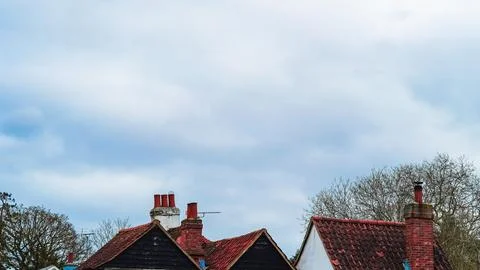 A cloudy blue sky over a small house rooftop with a chimney in an English tow Stock Photos