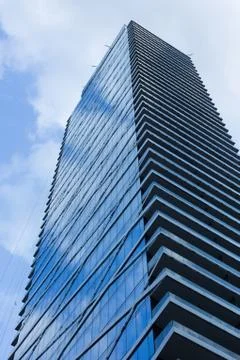 Cloudy blue sky reflection skyscraper glass exterior trees framing Stock Photos