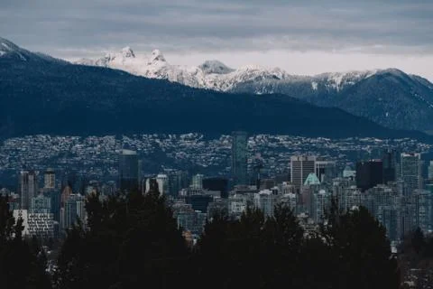 Cloudy cityscape with mountains in snow in background Stock Photos