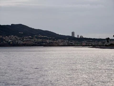 Cloudy coastal horizon featuring distant towers and foreground water enhancing Stock Photos