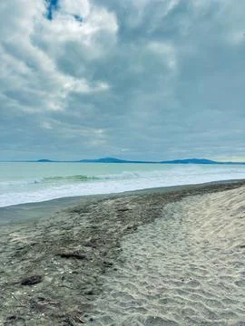 Cloudy day at the beach with waves and distant mountains in the background .. 写真素材