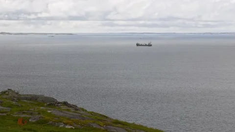 Cloudy day at ice sea beach. Small fishing vessel. Cargo ship sailing to Stock Footage 220320025