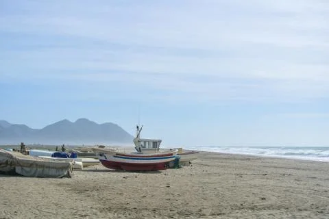Cloudy day at the lonely beach with colored boats on the shore not far from.. Stock Photos
