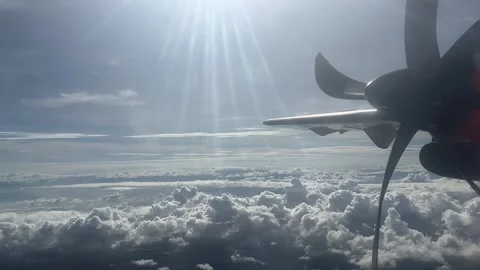 Cloudy day time sky through flying plane window sun flair  aircraft propellor Stock Footage 248960032