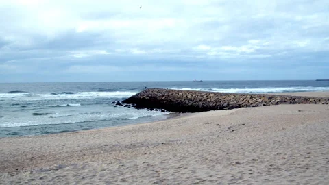 Cloudy Seascape with Sandy Beach, Ocean Waves, and Rocky Jetty Stock Footage 321889697