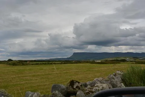 Cloudy Skies Over Rolling Fields and Distant Mountains in Scenic Landscape Foto stock