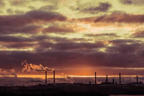 Cloudy sky with clouds during sunset and smoking chimneys of an aluminum plan Stock Photos