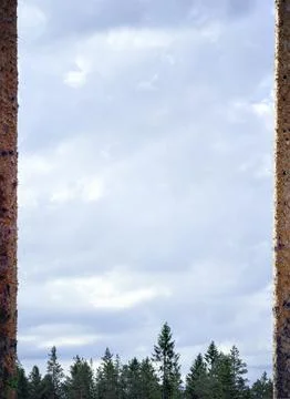 Cloudy sky framed by rough stone edges above a tree line Фото