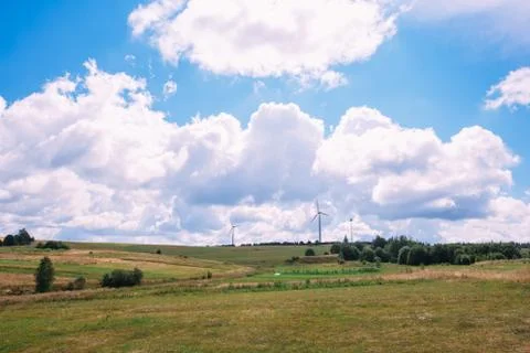 Cloudy sky with a hilly field on which wind generators stand Stock Photos