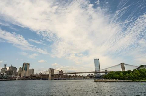 Cloudy sky over Brooklyn Bridge and skyline with water in foreground during.. 스톡 사진