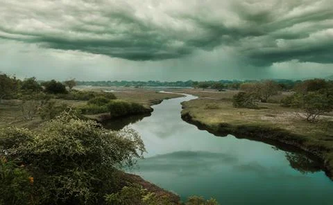 Cloudy sky over a calm river with partial vegetation on both banks Stock Photos