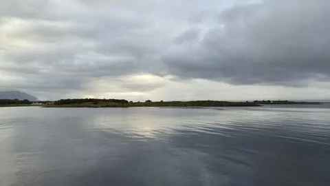 Cloudy sky over calm water with distant land in sight during the day Stock Photos