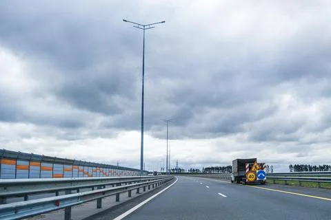 Cloudy sky over an empty highway leading to a curved road section with a truck Stock Photos