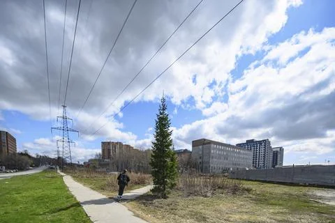 Cloudy sky over a high-voltage power line, buildings and a boy on a scooter Stock Photos