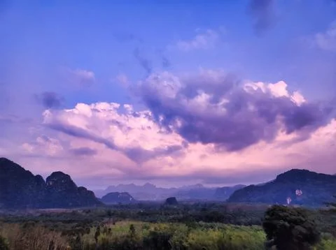 Cloudy sky over mountains at sunset in a rural area with green fields and t.. Stock Photos