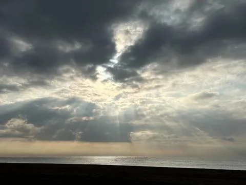 Cloudy sky over the ocean with sun rays breaking through Stock Photos