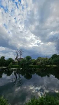 Cloudy sky over river with trees and reflection on water Stock Photos