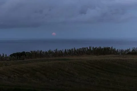 A cloudy sky with a red full moon in the background above the sea. Foto stock