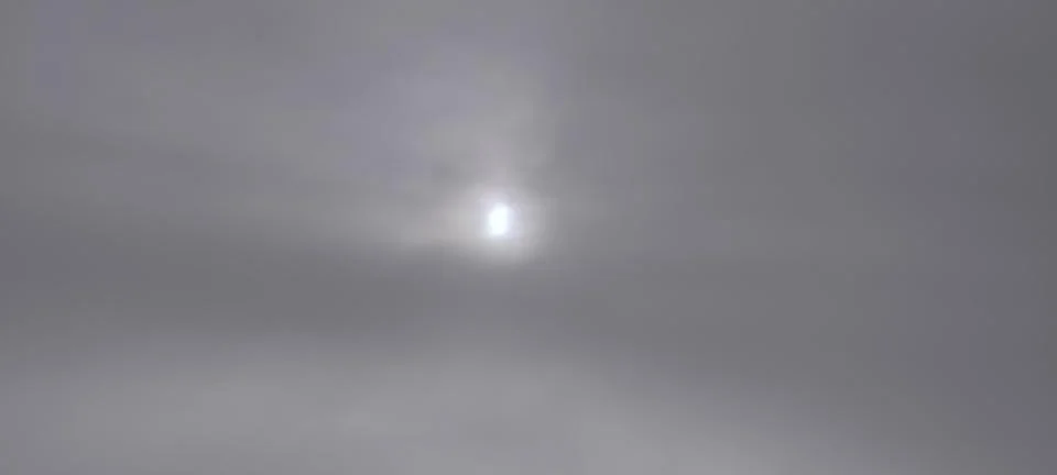 A cloudy sky with the sun partially hidden behind thick gray clouds Fotos de archivo