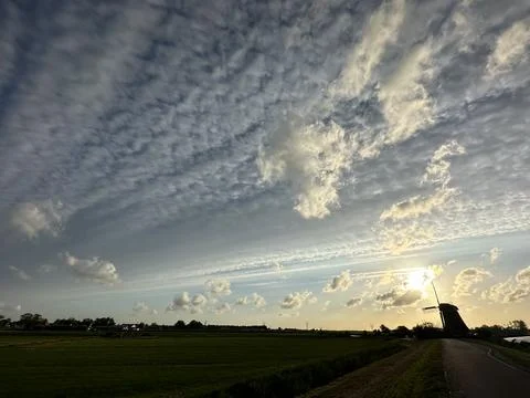 Cloudy sky at sunset silhouettes windmill in natural landscape Stock Photos