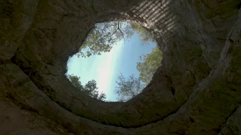 Cloudy sky through opening gap in cave ceiling. Camera look vertical up, pan Stock Footage 141954555