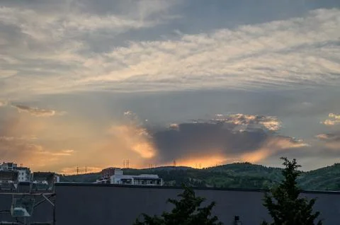 Cloudy Sunset Over City Skyline with Dramatic Sun Rays Breaking Through Cloud Stock Photos