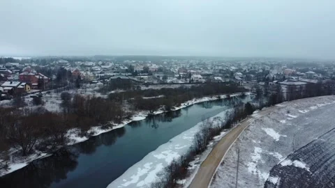 Cloudy winter day over river and town with snow covering houses and fields in ru Stock Footage 329708589