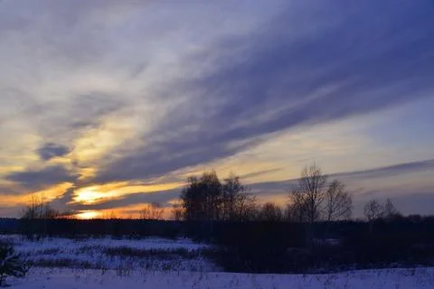 Cloudy winter sunset over snowy ground. Winter February evening. Stock Photos