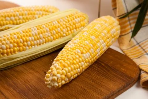 Clous up view of cutting board with three cobs sweet corn on white wooden b.. Stock Photos