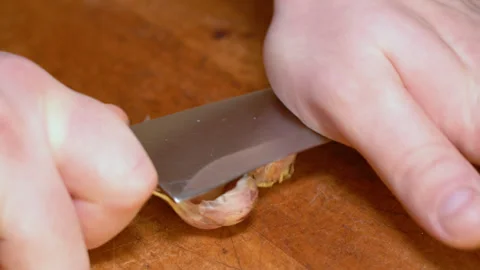 Clove of garlic is crushed on the kitchen table with a knife blade close-up Stock Footage 247830831