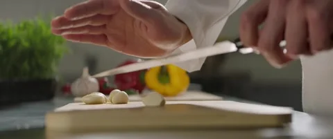 Clove of garlic is crushed on the kitchen table with a knife blade close-up Stock Footage 288144300