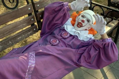 A clown with sharp teeth lies on a bench in a city park. The concept of fear  Stock Photos