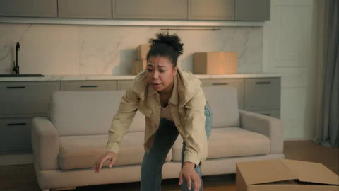 Clumsy African american woman falling cardboard boxes in living room frustrated Stock Footage 319092753