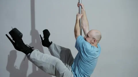 A clumsy and awkward man is trying to learn how to dance on a pole by rotating Stock Footage 305324644